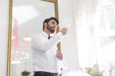 Elegant waiter in restaurant examining wine glass - WESTF020418