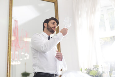 Eleganter Kellner im Restaurant, der ein Weinglas untersucht - WESTF020418