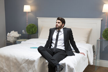Ernster Mann im Anzug sitzt auf dem Bett - WESTF020445
