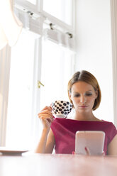 Frau hält Tasse und benutzt digitales Tablet - WESTF020472