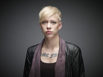Porträt einer blonden jungen Frau mit Tattoo vor grauem Hintergrund - RH000462