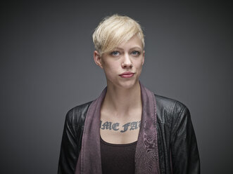 Porträt einer blonden jungen Frau mit Tattoo vor grauem Hintergrund - RH000463