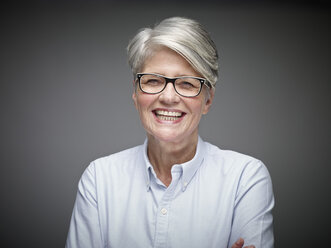 Porträt einer lachenden reifen Frau mit grauen Haaren vor einem grauen Hintergrund - RHF000467