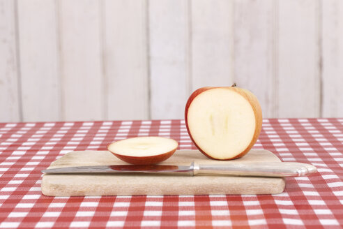 Aufgeschnittener Apfel und Messer auf hölzernem Küchenbrett und rot-weiß kariertem Tuch - DRF001220