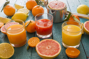 Gläser mit Orangensaft, Grapefruitsaft und Multivitaminsaft, Saftpresse und Früchte auf Holz - SARF001196