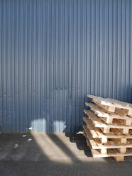 Stapel von Holzpaletten vor einer blauen Stahlblechfassade - JMF000304