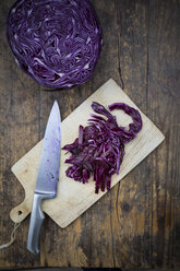 Red cabbage, knife and kitchen board on dark wood - LVF002528