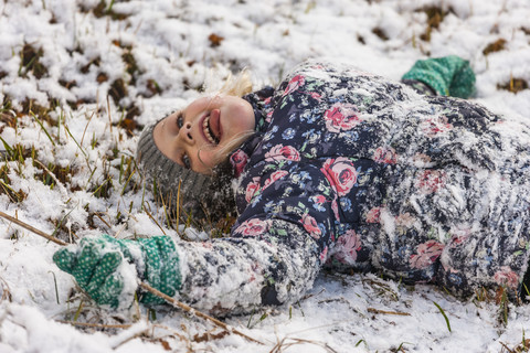 Kleines Mädchen mit herausgestreckter Zunge auf schneebedeckter Wiese liegend, lizenzfreies Stockfoto