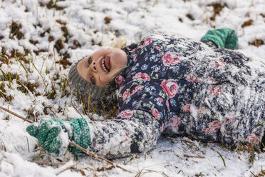 Kleines Mädchen mit herausgestreckter Zunge auf schneebedeckter Wiese liegend - TCF004476