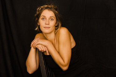 Portrait of woman wearing black corsage leaning on back rest in front of black background - TCF004467