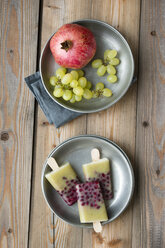 Gerichte mit selbstgemachten Trauben-Granatapfel-Popsicles, grünen Trauben und Granatapfel auf Holz - MYF000780