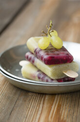 Teller mit einem Stapel selbstgemachter Trauben-Granatapfel-Eis am Stiel und grünen Trauben - MYF000782