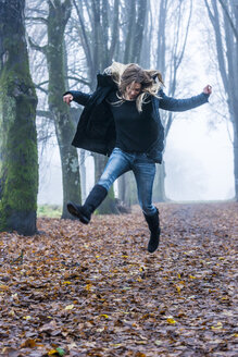 Frau springt auf einem Waldweg in die Luft - TCF004496