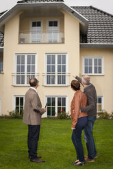 Immobilienmakler mit Kaufinteressenten vor einem Wohnhaus - PAF001116