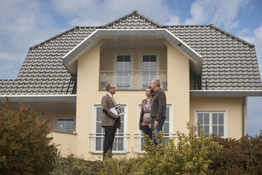 Immobilienmakler im Gespräch mit potenziellen Käufern vor einem Wohnhaus - PAF001120