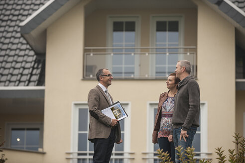 Immobilienmakler im Gespräch mit potenziellen Käufern vor einem Wohnhaus - PAF001121