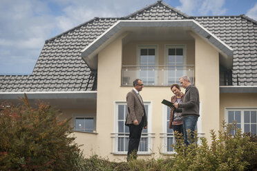 Immobilienmakler mit Kaufinteressenten vor einem Wohnhaus - PAF001153