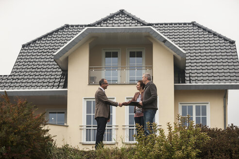 Immobilienmakler schüttelt potenziellen Käufern vor einem Wohnhaus die Hand - PAF001122