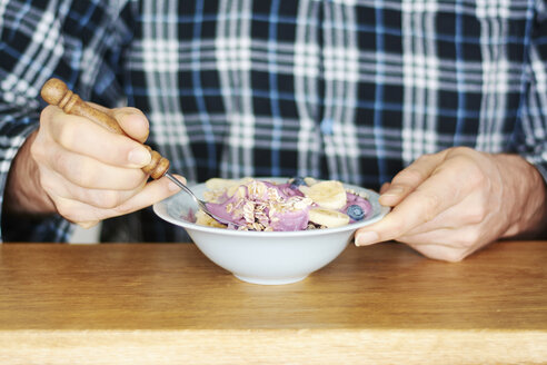 Mann im Pyjama isst Müsli mit Sojajoghurt, Blaubeeren und Banane - HAWF000547