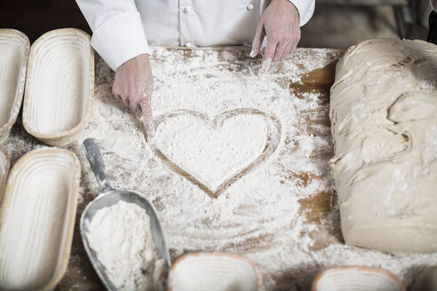 Female baker drawing heart in flour on a wooden table top - ZEF003793