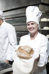 Bäckerin freut sich über frisch gebackenes Brot aus dem Ofen - ZEF003804