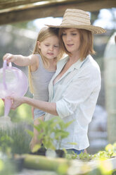 Portrait of woman and little daughter watering plants with watering can - ZEF004066