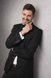 Portrait of smiling man wearing dinner jacket and bow leaning at wall - SHKF000104