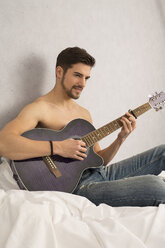 Hemdloser Mann mit Gitarre auf dem Bett sitzend - SHKF000115