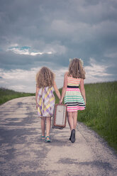 Germany, Bavaria, Two girl walking on country road carrying old suitcase, rear view - VTF000381