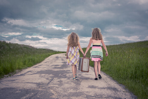 Germany, Bavaria, Two girl walking on country road carrying old suitcase, rear view - VTF000382