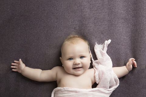 Smiling baby girl with outstretched arms lying on blanket stock photo