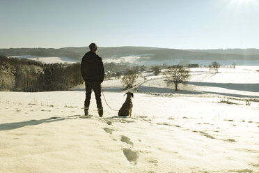 Germany, Bergisches Land, man walking dog in winter landscape - ONF000753