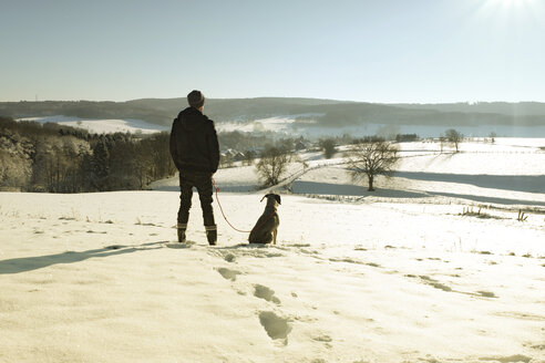 Deutschland, Bergisches Land, Mann geht mit Hund in Winterlandschaft spazieren - ONF000753