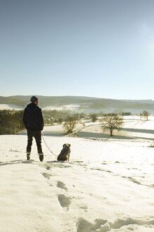 Deutschland, Bergisches Land, Mann geht mit Hund in Winterlandschaft spazieren - ONF000735