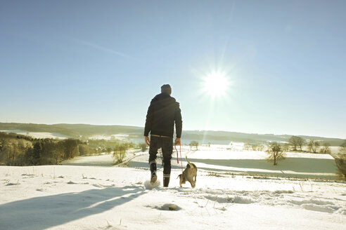 Deutschland, Bergisches Land, Mann geht mit Hund in Winterlandschaft spazieren - ONF000754