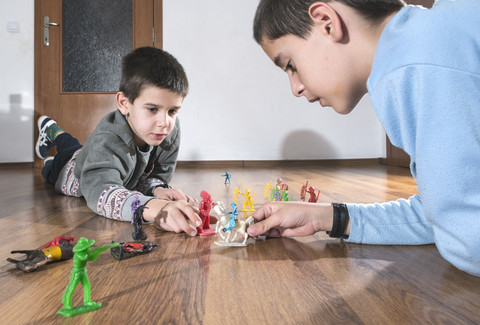 Zwei Jungen spielen zu Hause mit Miniaturfiguren auf dem Boden, lizenzfreies Stockfoto