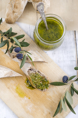 Aufgeschnittenes selbstgebackenes Baguette mit frischem Basilikum-Pesto und Olivenzweigen auf Holzbrett, lizenzfreies Stockfoto