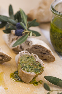 Aufgeschnittenes selbstgebackenes Baguette mit frischem Basilikum-Pesto und Olivenzweigen auf Holzbrett - ODF000979