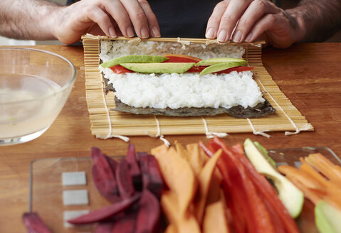 Mann rollt Sushi mit einer Füllung aus Süßkartoffeln, Avocado und Paprika - HAWF000562