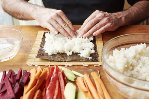 Mann, der Reis auf einem Nori-Blatt ausbreitet, um Gemüse-Sushi zu machen - HAWF000563