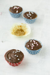 Vier Cupcakes mit Schokoladen- und Zuckerperlen und einem leeren Pappbecher - MYF000792