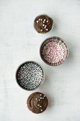 Two cupcakes with chocolate cream and sugar pearls and two bowls of sugar pearls - MYF000795