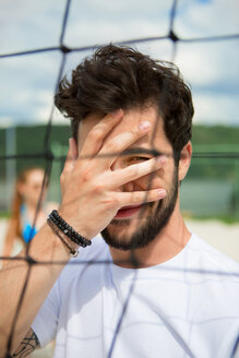 Junger Mann bedeckt sein Gesicht am Netz des Beachvolleyballfeldes - WESTF020679