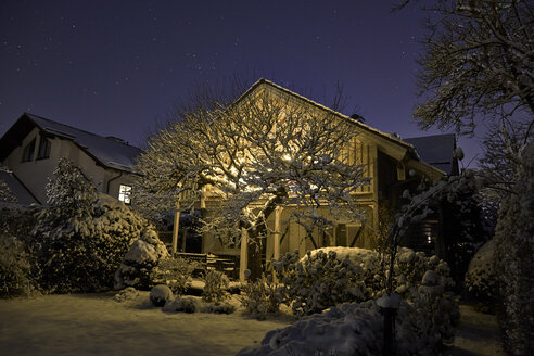 Deutschland, beleuchtetes Einfamilienhaus mit schneebedecktem Garten im Vordergrund - KDF000527