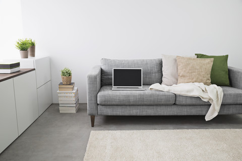Geöffneter Laptop auf der Couch im modernen Wohnzimmer, lizenzfreies Stockfoto