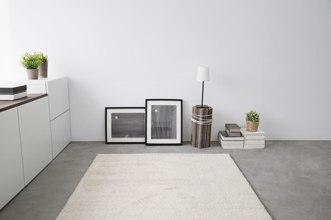 Sideboard, Bilderrahmen, Bücherstapel, Teppich und Tischlampe in einem modernen Wohnzimmer, lizenzfreies Stockfoto