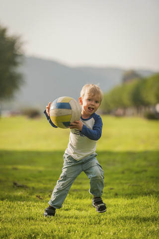 Junge hält Ball auf Wiese, lizenzfreies Stockfoto