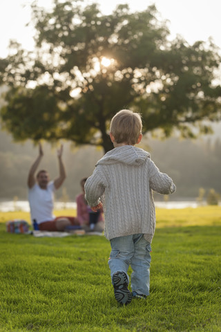 Junge läuft auf einer Wiese auf seine Familie im Hintergrund zu, lizenzfreies Stockfoto