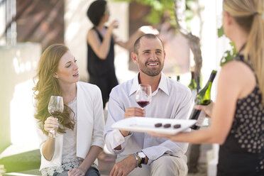 Kellnerin mit Tablett und Paar, das im Freien sitzt und Rotwein probiert - ZEF003195
