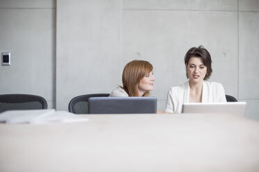 Two businesswomen using laptops in conference room - ZEF003043